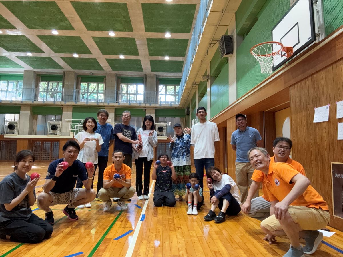 千川小学校体育館で、参加者がボッチャのボールを持って並んでいる集合写真