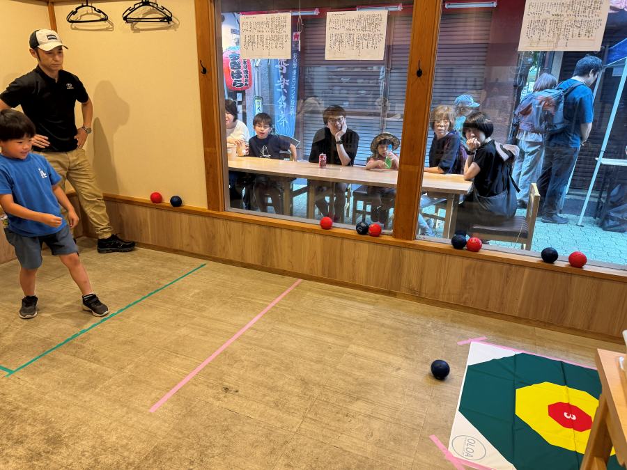 ザキ屋の店内コートで、子どもがボッチャのボールを投げる様子を見守る参加者たち