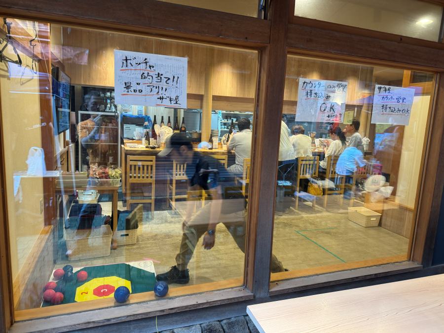 ザキ屋の店先に貼られた「ボッチャ的当て」の手書きポスターと、店内で投球するスタッフ